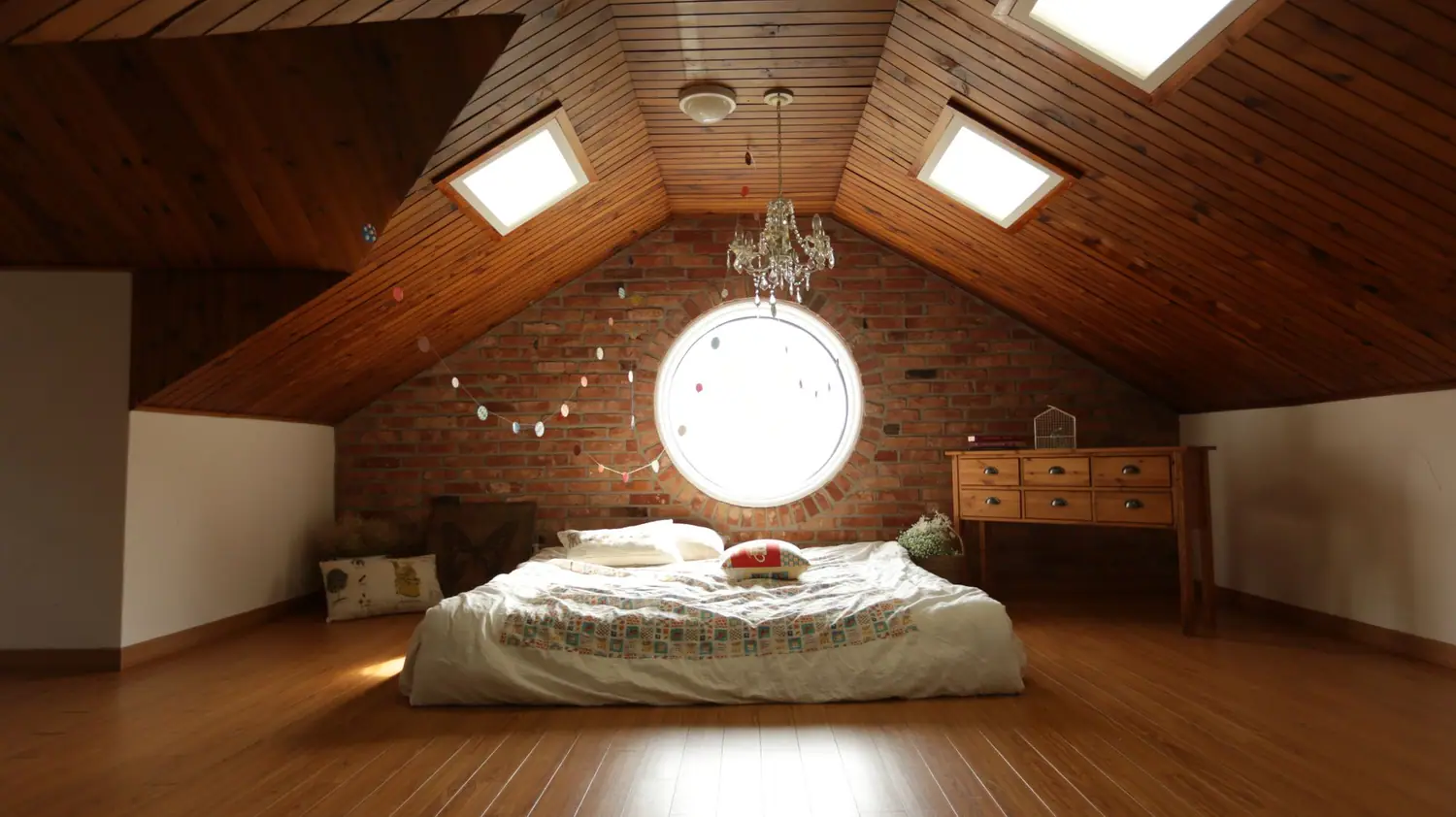 Bedroom under a sloped wood ceiling with a round window and a low dresser