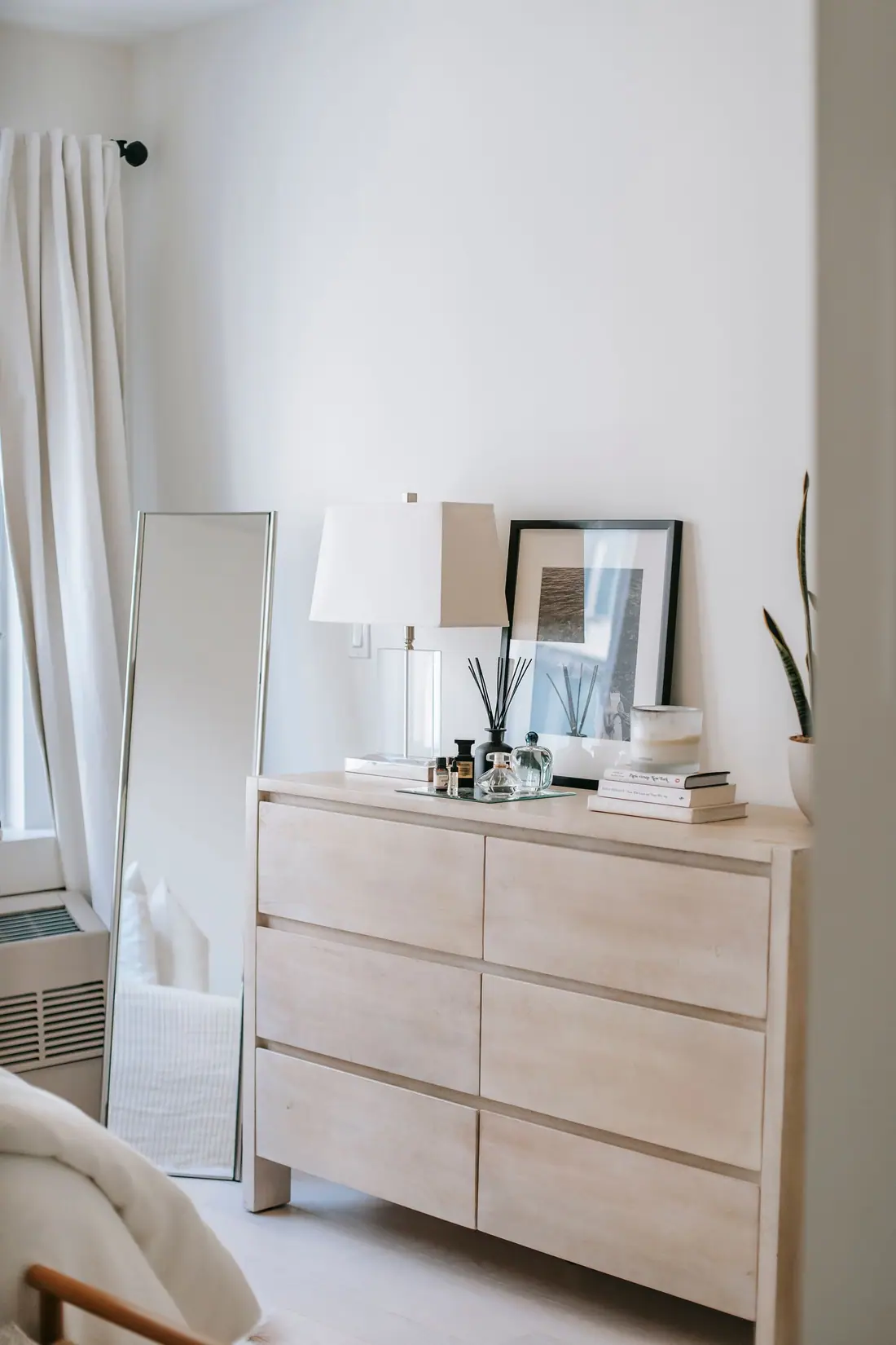 Light wood six-drawer dresser against a bedroom wall beside a leaning mirror