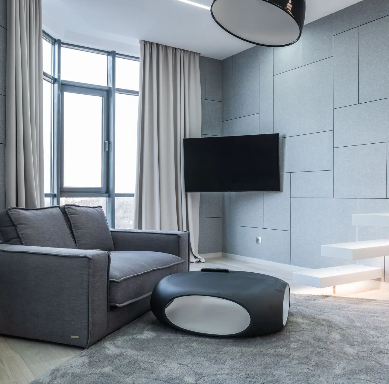 Gray sofa, oval coffee table, and a television mounted on a paneled wall