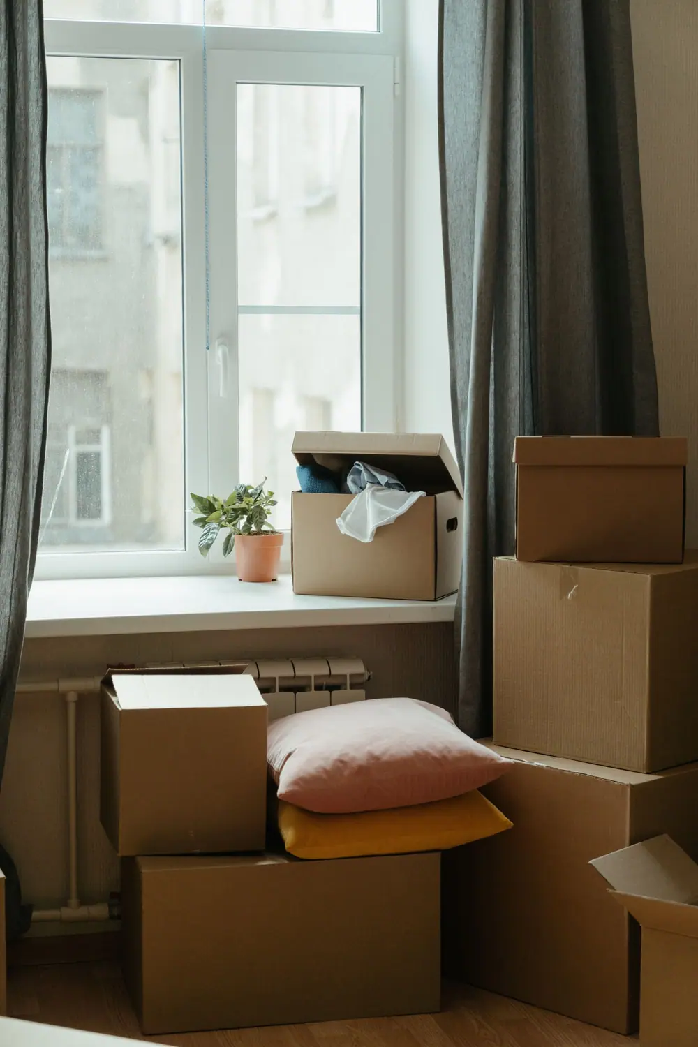 Cardboard cartons and cushions stacked beside a window and a radiator