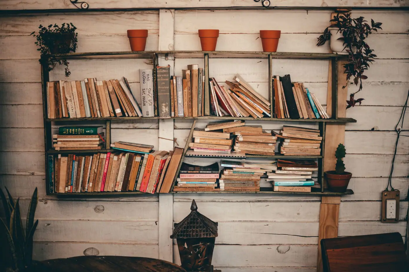 A long wooden shelf of books mounted on a white plank wall