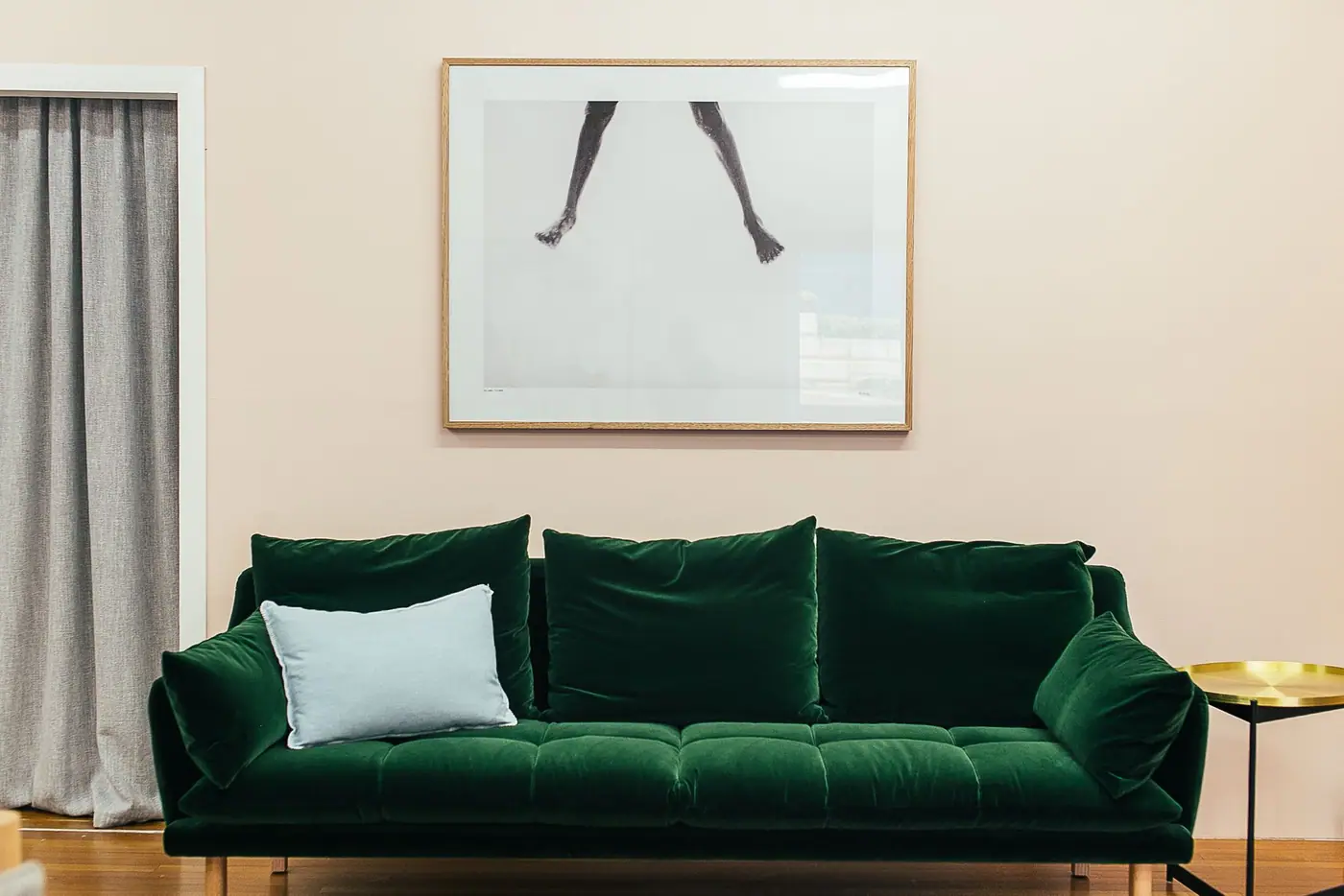 Green velvet sofa under a large framed photograph, with a doorway and curtain at the left